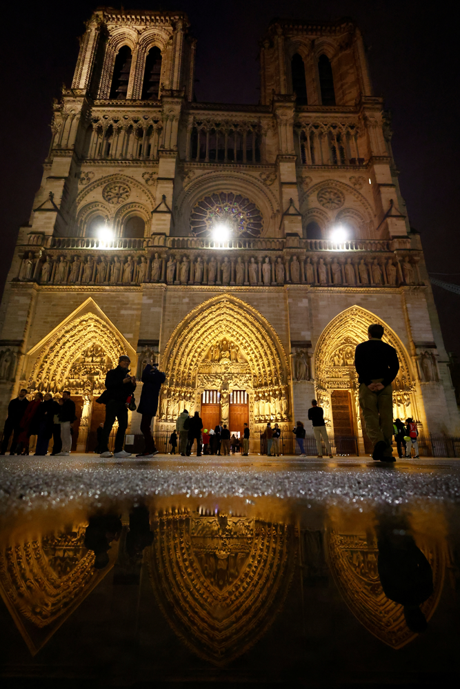 The Notre-Dame de Paris Cathedral is reflected in a puddle as people arrive to attend a mass open to the public as part of ceremonies to mark the Cathedral's reopening after its restoration, five-and-a-half years after a fire ravaged the Gothic masterpiece, in Paris, France, December 8, 2024. REUTERS/Christian Hartmann