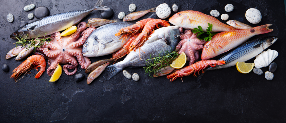 Fresh fish and seafood assortment on black slate background. Copy space. Top view.